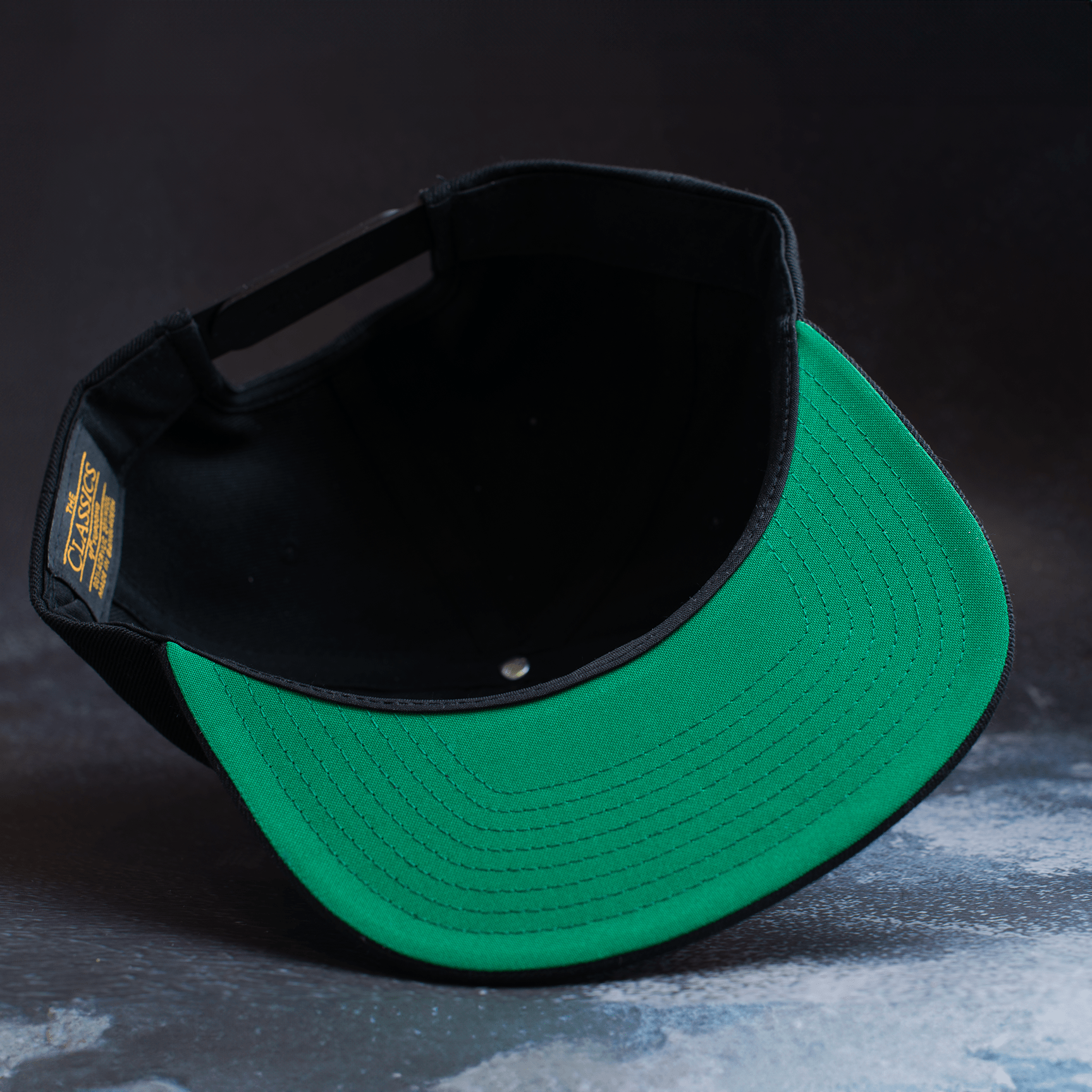 Black snapback hat with embroidered Fa Ram logo patch on the front. Bottom of hat view.