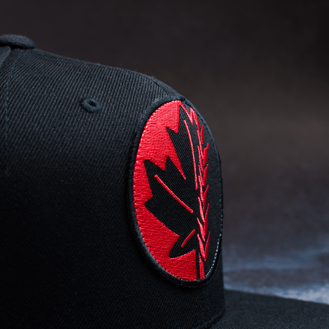 Black snapback hat with embroidered Fa Ram logo patch on the front. Close up of patch from left side.