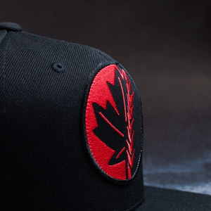 Black snapback hat with embroidered Fa Ram logo patch on the front. Close up of patch from left side.